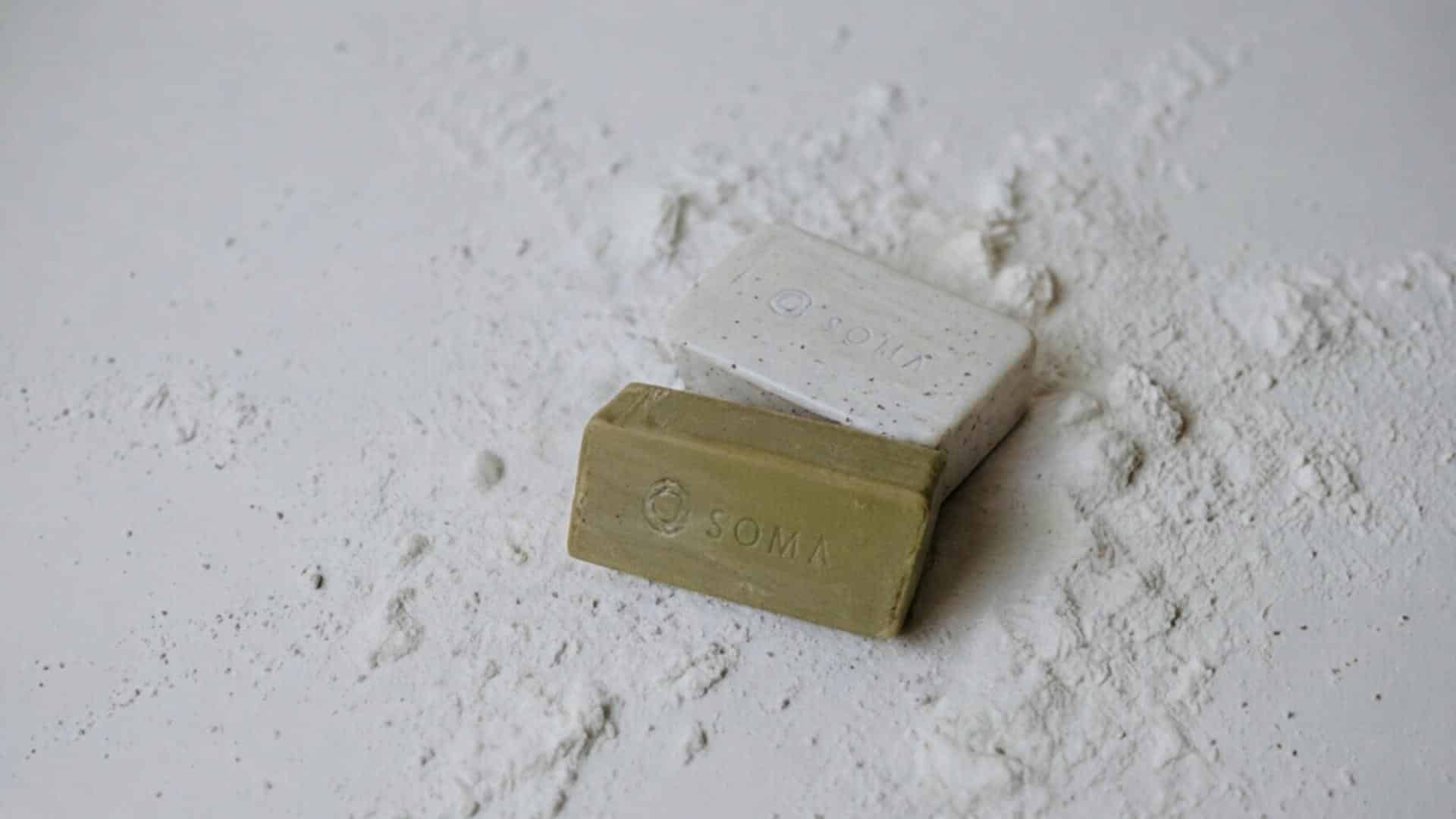 Dos jabones SOMA con su marca grabada, sobre una superficie de polvo blanco.